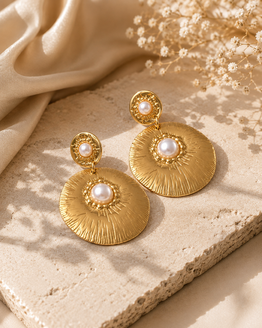 Solara Pearl Drops – gold-tone stainless steel statement earrings featuring textured sunburst discs with elegant faux pearl centers on a neutral luxury background.