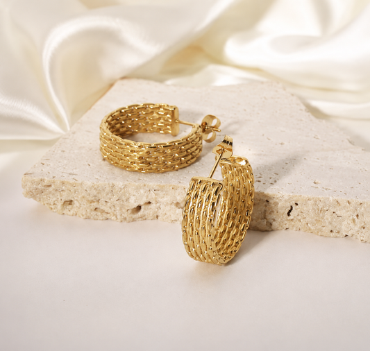 gold-tone stainless steel woven hoop earrings with a textured braided design displayed on a luxury neutral stone background.