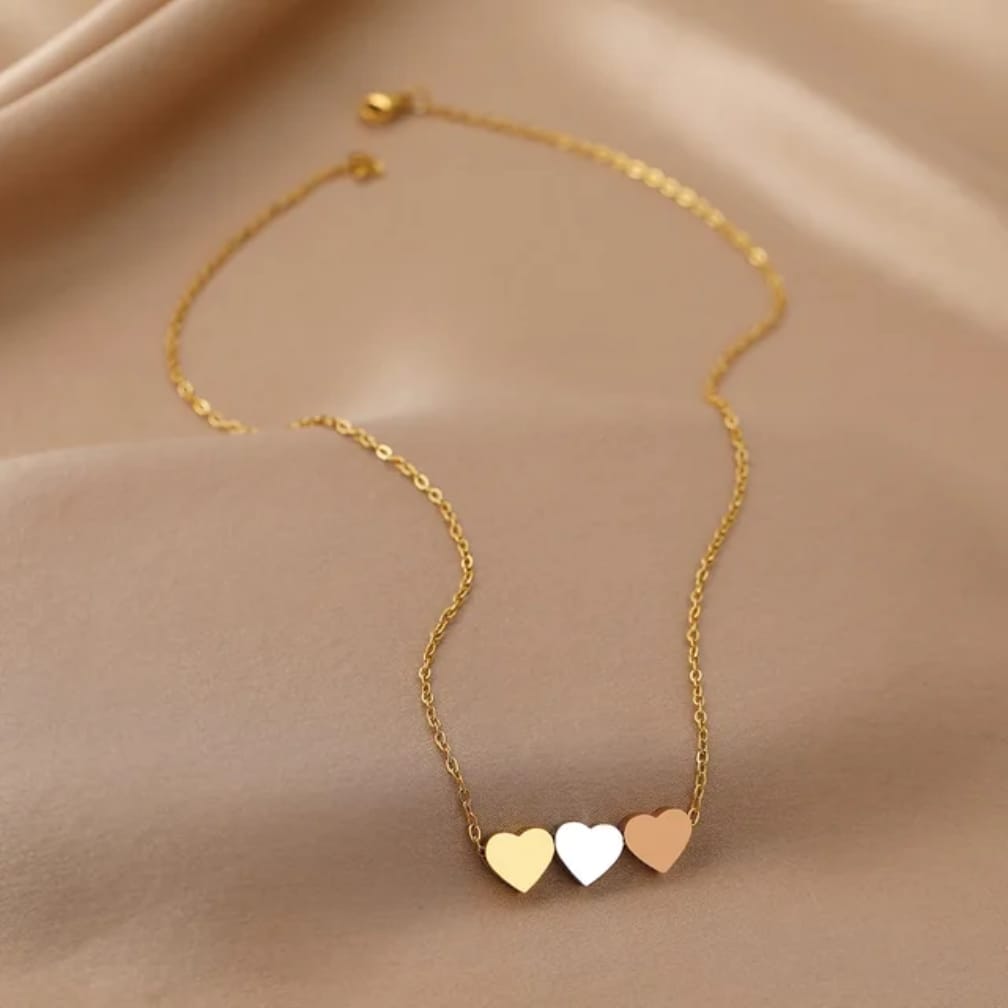 A delicate gold chain necklace featuring three small, polished heart pendants in gold, white, and rose gold,