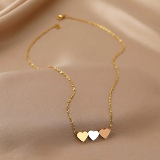 A delicate gold chain necklace featuring three small, polished heart pendants in gold, white, and rose gold,
