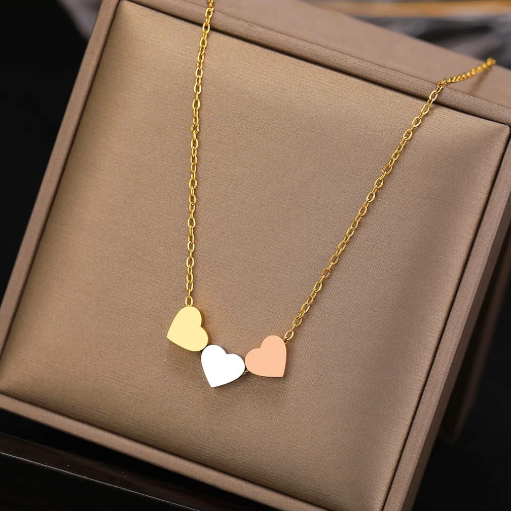 Gold necklace with three heart-shaped pendants on a brown jewelry box.