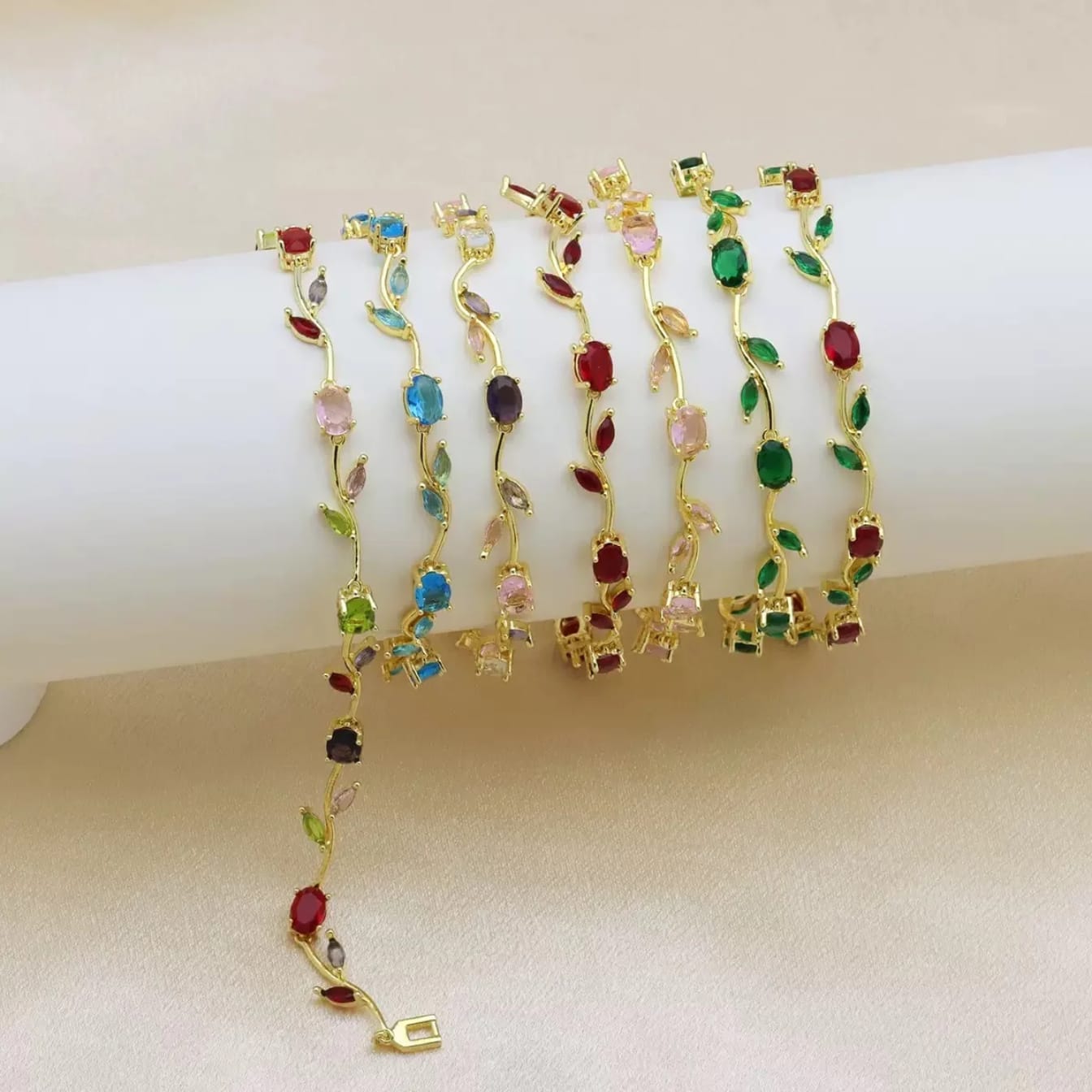 Set of gold tulip bracelets with colorful gemstones on a beige surface